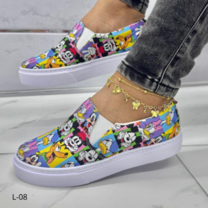 Tenis slip-on con estampado multicolor de personajes de Disney y suela blanca de plataforma, mostrados de perfil en una persona con jeans.